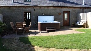 A stone building with a hot tub, outdoor seating, and a grassy yard.