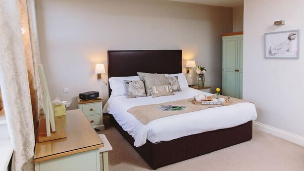 A neatly arranged bedroom with a large bed, bedside tables, a nightstand, a desk, and a wardrobe.