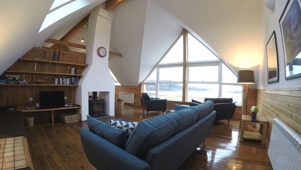 A spacious loft with a large window, wooden floors, a sofa, and a TV. - Windyhill Lodge 14665 (Ullapool)