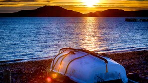 A boat tied to a rocky shore with a sunset in the background. - Windyhill Lodge 14665 (Ullapool)