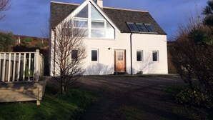 A two-story house with a sloped roof, a large window on the upper floor, and a front door. - Windyhill Lodge 14665 (Ullapool)