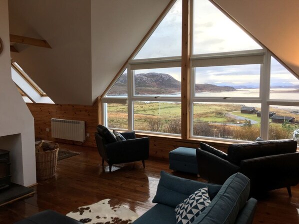 A spacious loft with a large skylight, wooden floors, and a view of a lake and mountains. - Windyhill Lodge 14665 (Ullapool)