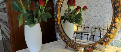 A bathroom vanity with a white marble countertop, a white vase with red roses, and a mirror with an ornate gold frame.