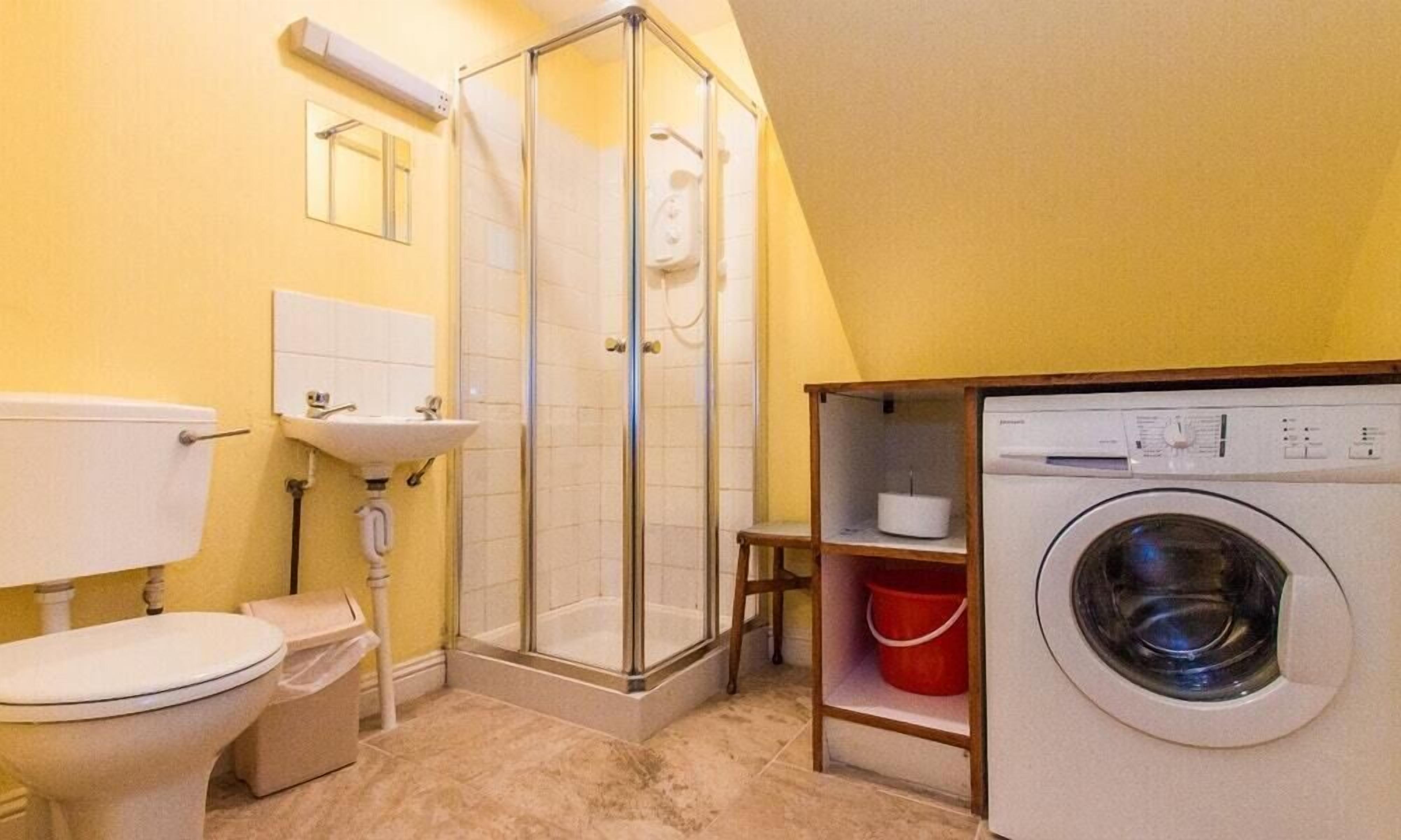 Casa de banho compacta com sanita, lavatório, chuveiro e máquina de lavar roupa.