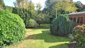 A well-maintained garden with various shrubs and trees, a clear pathway, and a building with a sloped roof. - Surima, Chichester 48663 (Chichester)