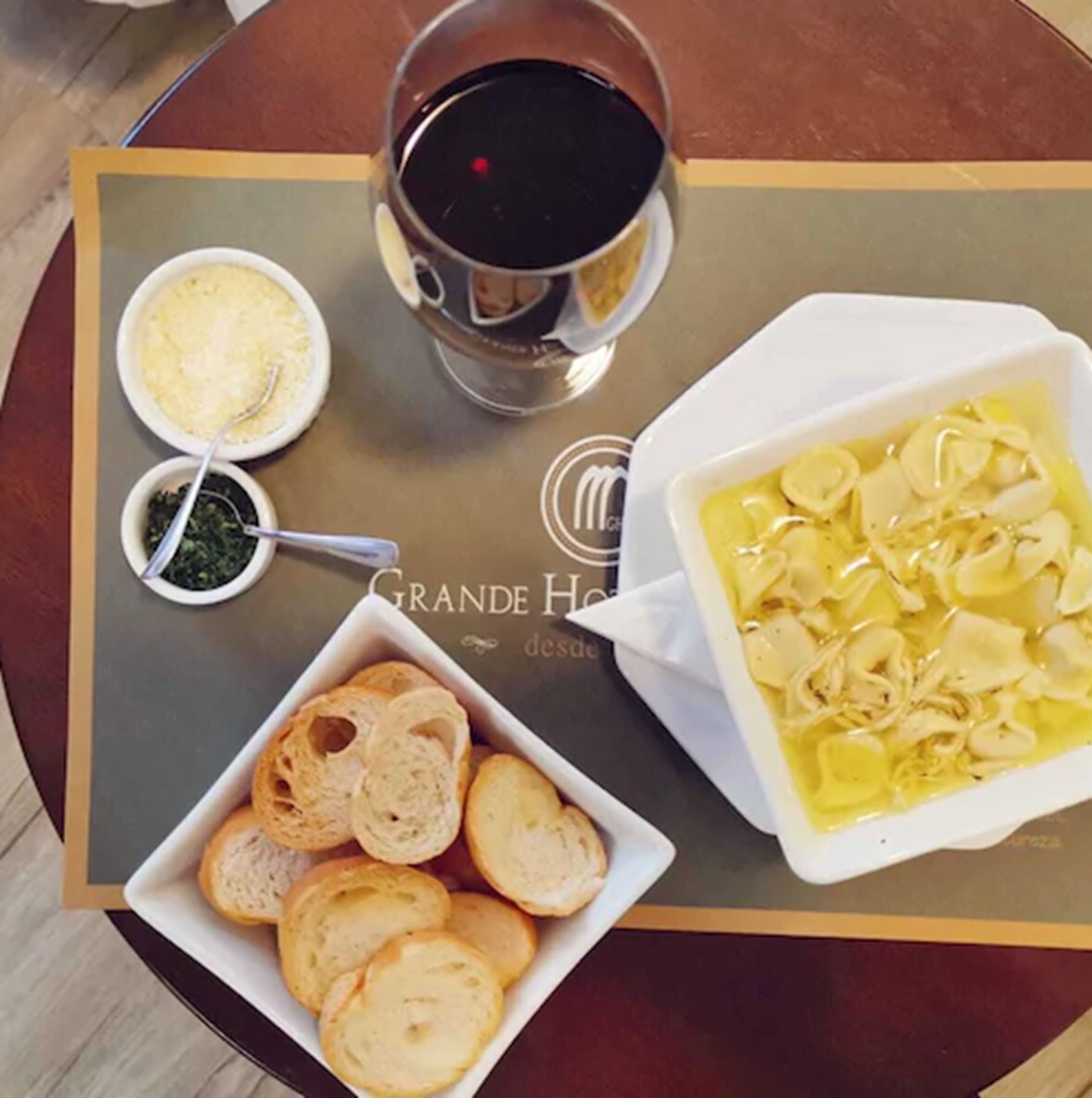 A dining table with a plate of bread, a bowl of soup, and a glass of red wine.
