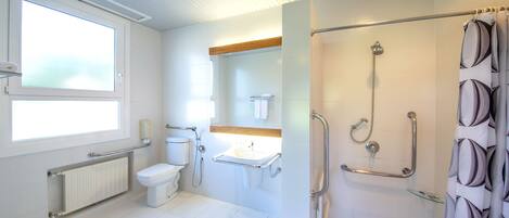 A modern bathroom with a toilet, sink, and shower. It includes a window, a towel rack, and a handrail for accessibility.