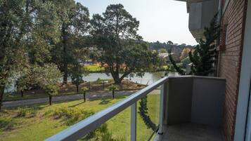 Un balcon avec vue sur un lac, des arbres et un bâtiment en briques.
