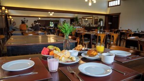 Un desayuno con diversos platos, como waffles, fruta y jugo de naranja, sobre una mesa de madera en un restaurante.