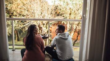 A couple sitting on a balcony with a view of trees and a brick wall.