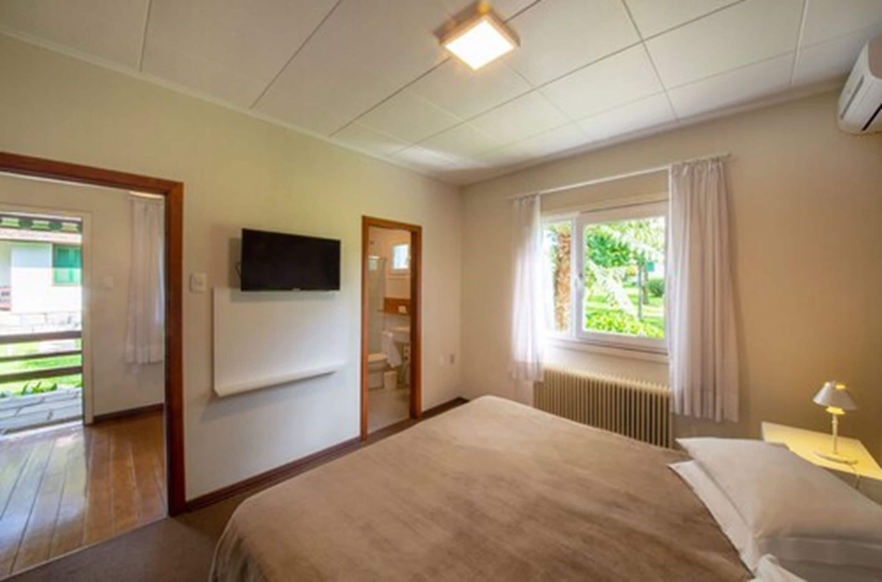 Habitación de hotel con cama, televisión montada en la pared, ventana con cortinas y vistas al exterior.
