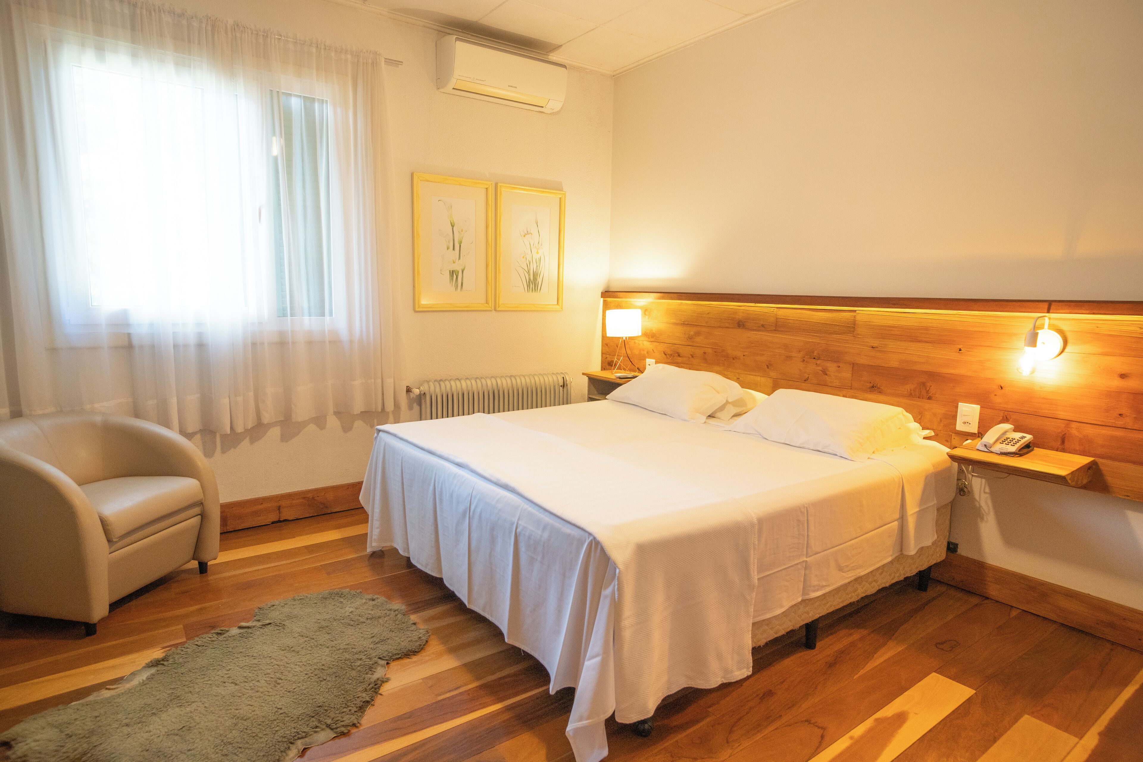 Habitación de hotel con cama, una silla, cabecero de madera, mesita de noche y teléfono en la pared.