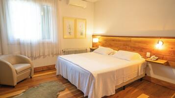 Habitación de hotel con cama, una silla, cabecero de madera, mesita de noche y teléfono en la pared.