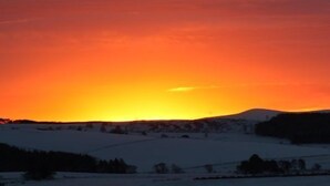 A snowy landscape with rolling hills and a sunset.