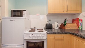 A compact kitchen with a white refrigerator, stove, and microwave. There are wooden cabinets and a granite countertop. - Nursery (Isle of Colonsay)