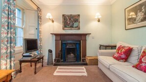 A living room with a fireplace, a sofa, a television, and a painting on the wall. - Nursery (Isle of Colonsay)