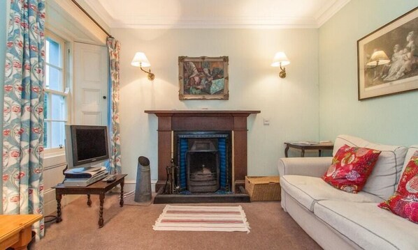 A living room with a fireplace, a sofa, a television, and a painting on the wall.