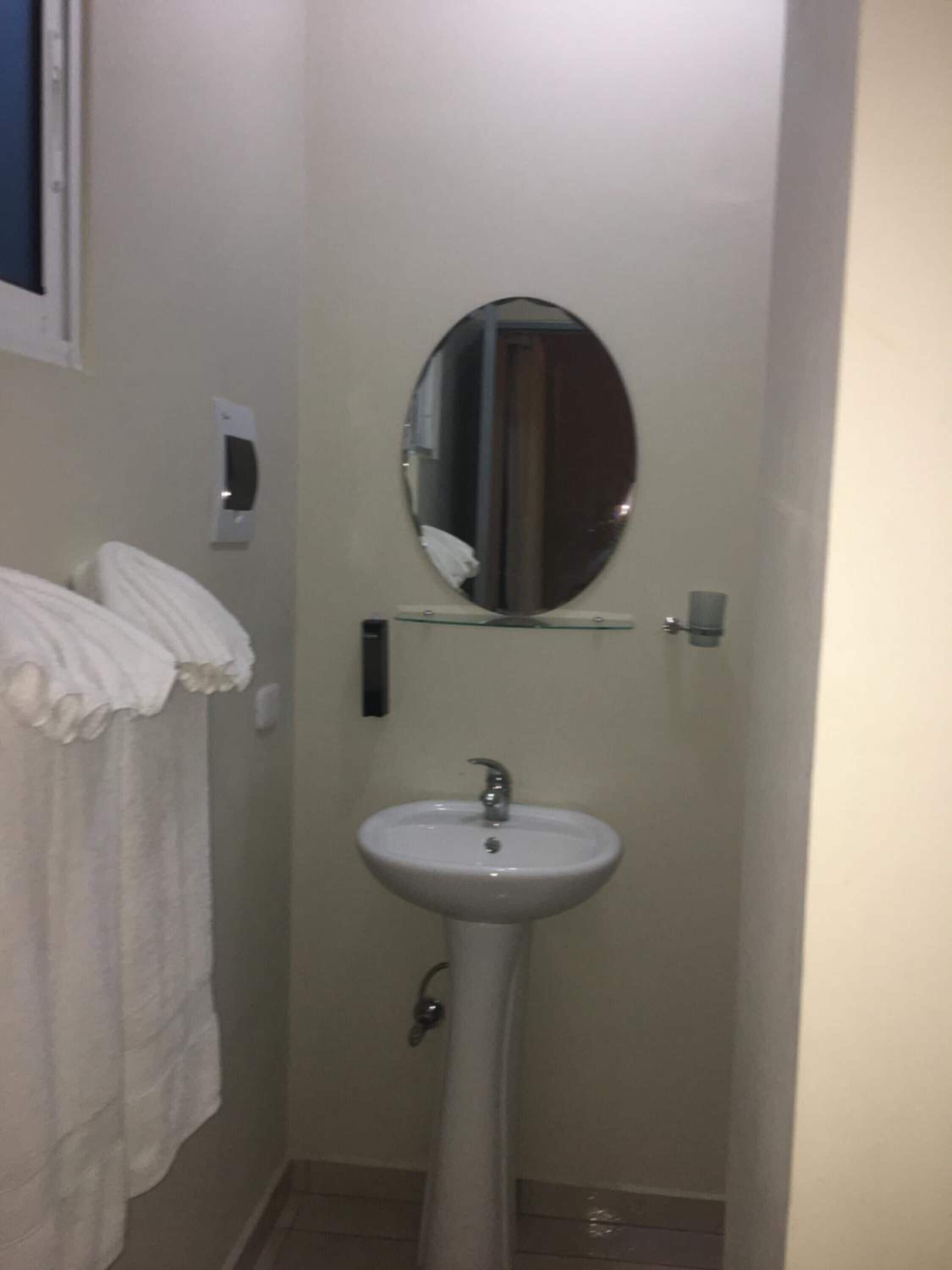 Un baño pequeño con un lavamanos pedestal, un espejo encima y una toalla colgada en la pared.