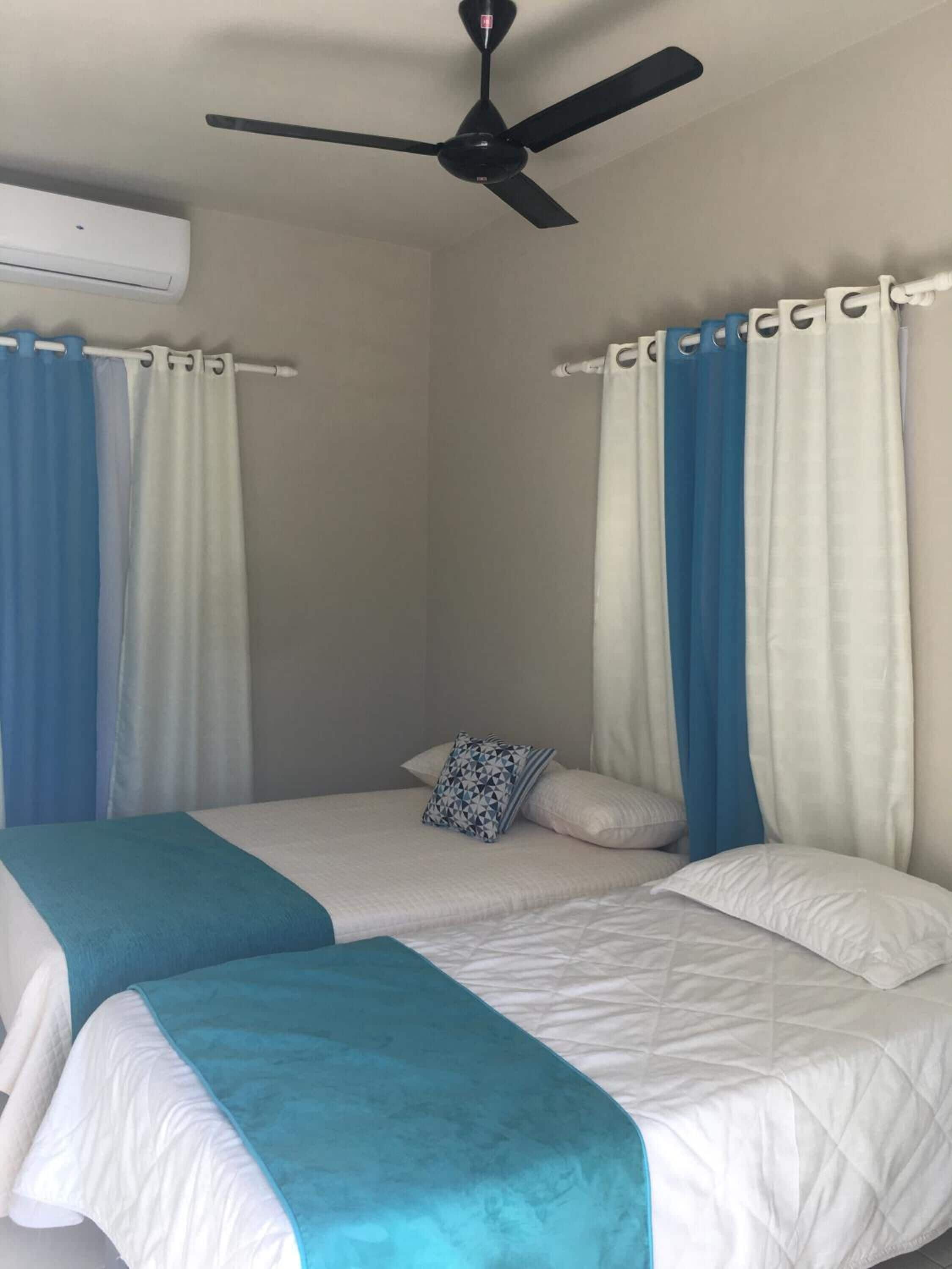 A bedroom with two beds, a ceiling fan, and curtains.