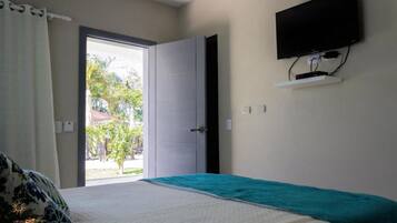 Un dormitorio con cama, televisor montado en la pared y puerta que da a un espacio exterior.