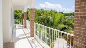 A balcony with a white railing, brick pillars, and lush green foliage in the background. - Hotel Casa Pierretta (Las Terrenas)
