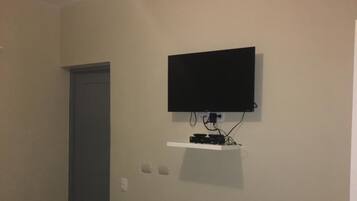 Una habitación con televisión montada en la pared, una puerta y una cama con colcha verde y azul.