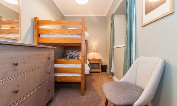 A bunk bed with a wooden frame, a dresser with drawers, a bedside table with a lamp, and a chair.