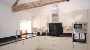 A modern kitchen with white cabinets, a black countertop, stainless steel appliances, and a wooden beam ceiling. - The Run, West Lavant 173744 (Chichester)