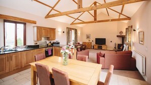 A spacious living area with a wooden dining table, a sofa set, and a television. - Watson Cottage (Hot Tub) (Brampton)