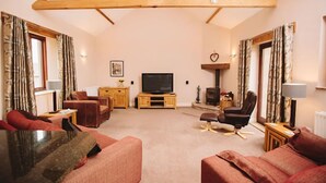 A living room with a wooden ceiling, a television, a fireplace, and a sofa. - Watson Cottage (Hot Tub) (Brampton)