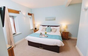A bedroom with a bed, bedside tables, a window with curtains, and a wall-mounted artwork. - Watson Cottage (Hot Tub) (Brampton)
