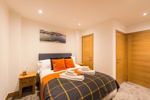 A neatly made bed with a plaid blanket, a bedside table with a lamp, and a wooden door. - Taymouth Marina  - No. 7 Lawers View (Aberfeldy)