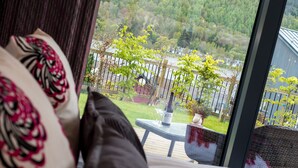 A bedroom with a large window overlooking a garden and a forested area.