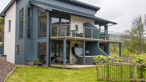 A modern two-story house with a balcony, large windows, and a well-maintained lawn.