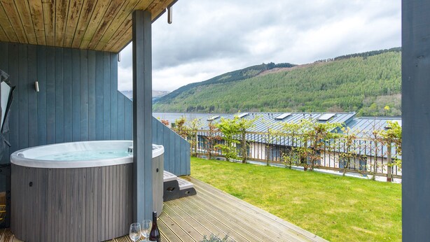 A hot tub on a wooden deck with a view of a lake and hills.