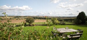 Een tuin met een houten tafel en stoelen, omgeven door groen en uitzicht op het landschap.