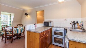 A compact kitchen with a microwave, stove, and sink. There is a wooden chair and a table with a striped tablecloth. - Turnigil (Isle of Colonsay)