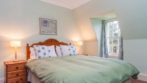 A bedroom with a wooden bed, two bedside tables with lamps, a map on the wall, and a window with curtains. - Turnigil (Isle of Colonsay)