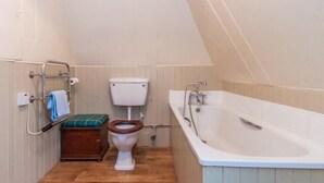 A small, compact bathroom with a toilet, a wooden seat, a bathtub, and a towel rack. - Turnigil (Isle of Colonsay)