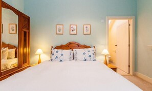 Quarto com cama de madeira, duas luminárias de cabeceira e três quadros florais na parede.