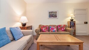 A living room with a beige sofa, a wooden coffee table, and two lamps. - Scalasaig Farmhouse (Isle of Colonsay)
