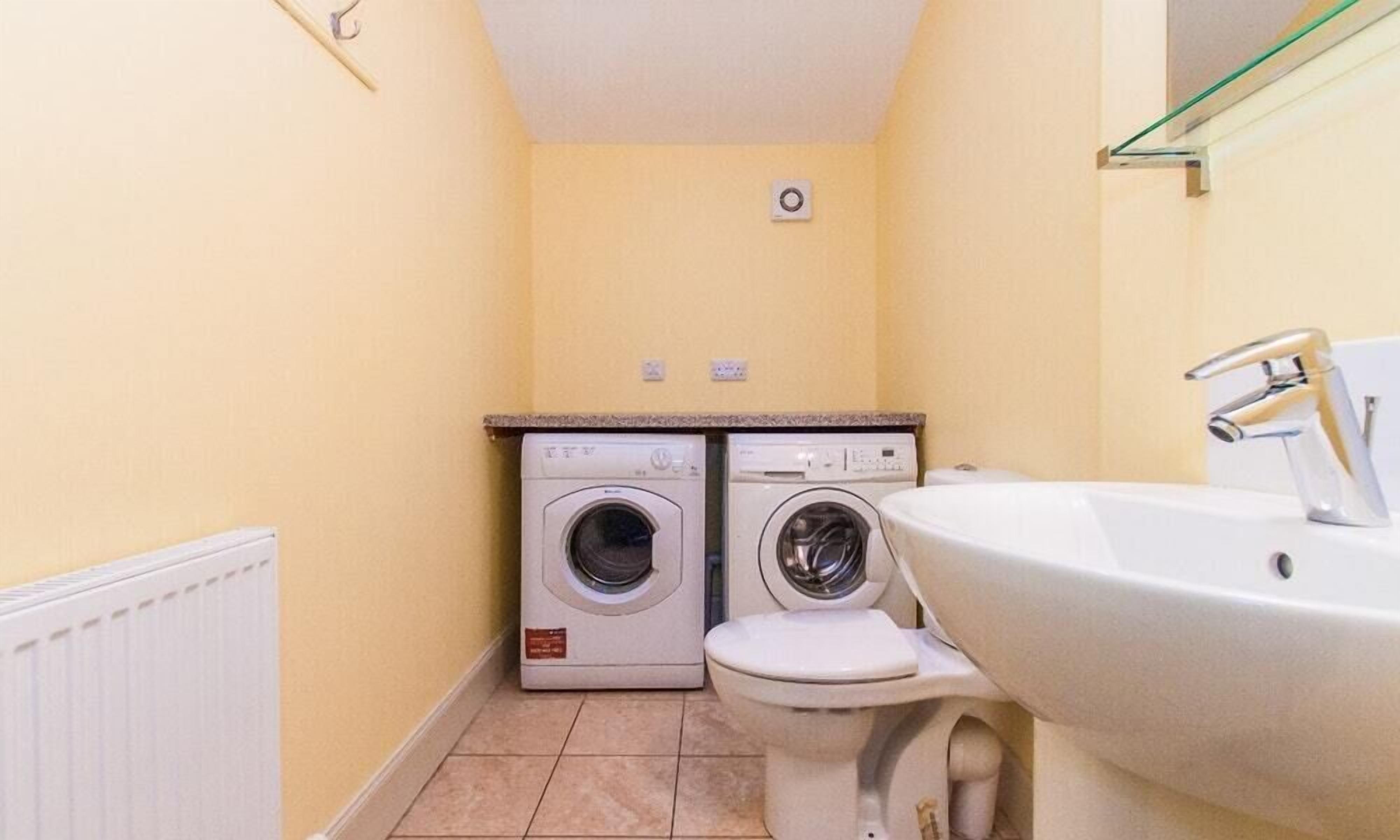 A compact bathroom with a white sink, two wall-mounted washing machines, and a toilet.