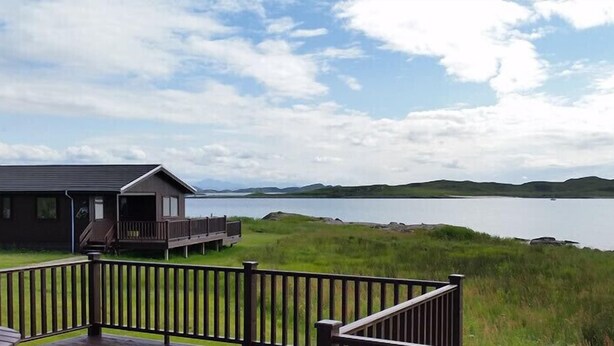 A lakeside cabin with a deck and a view of the lake and hills. - Cedar (Ullapool)