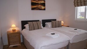 A double bed room with two bedside tables, each with a lamp, a painting on the wall, and a window with curtains.