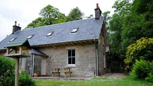 A stone house with a sloped roof, a small porch, and a picnic table. - Craigendarroch 2 (Oban)