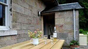 A wooden table with a white pitcher of flowers, two wine glasses, and a bottle of wine.