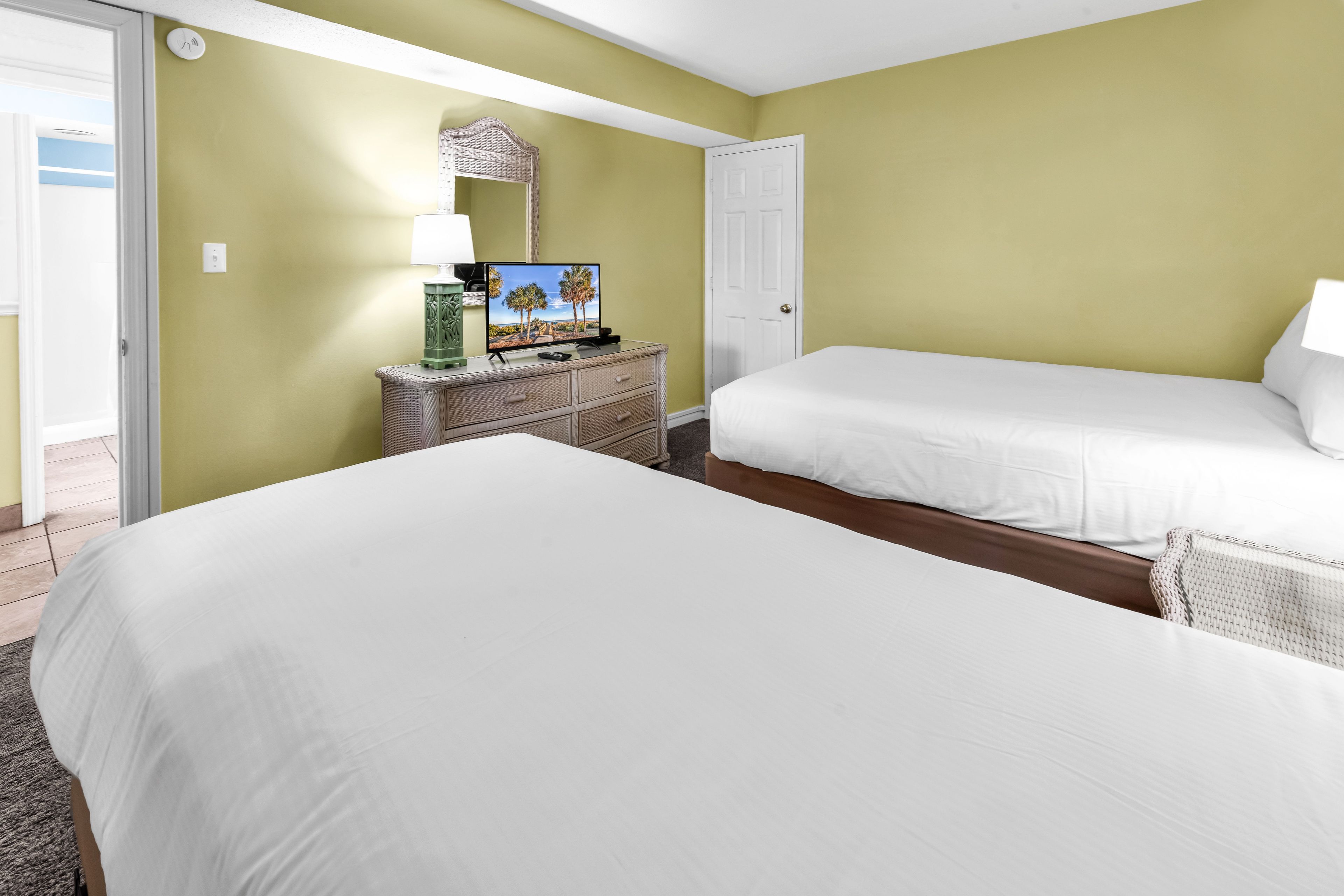 Una habitación de hotel con dos camas, un televisor sobre una mesita auxiliar y una puerta.