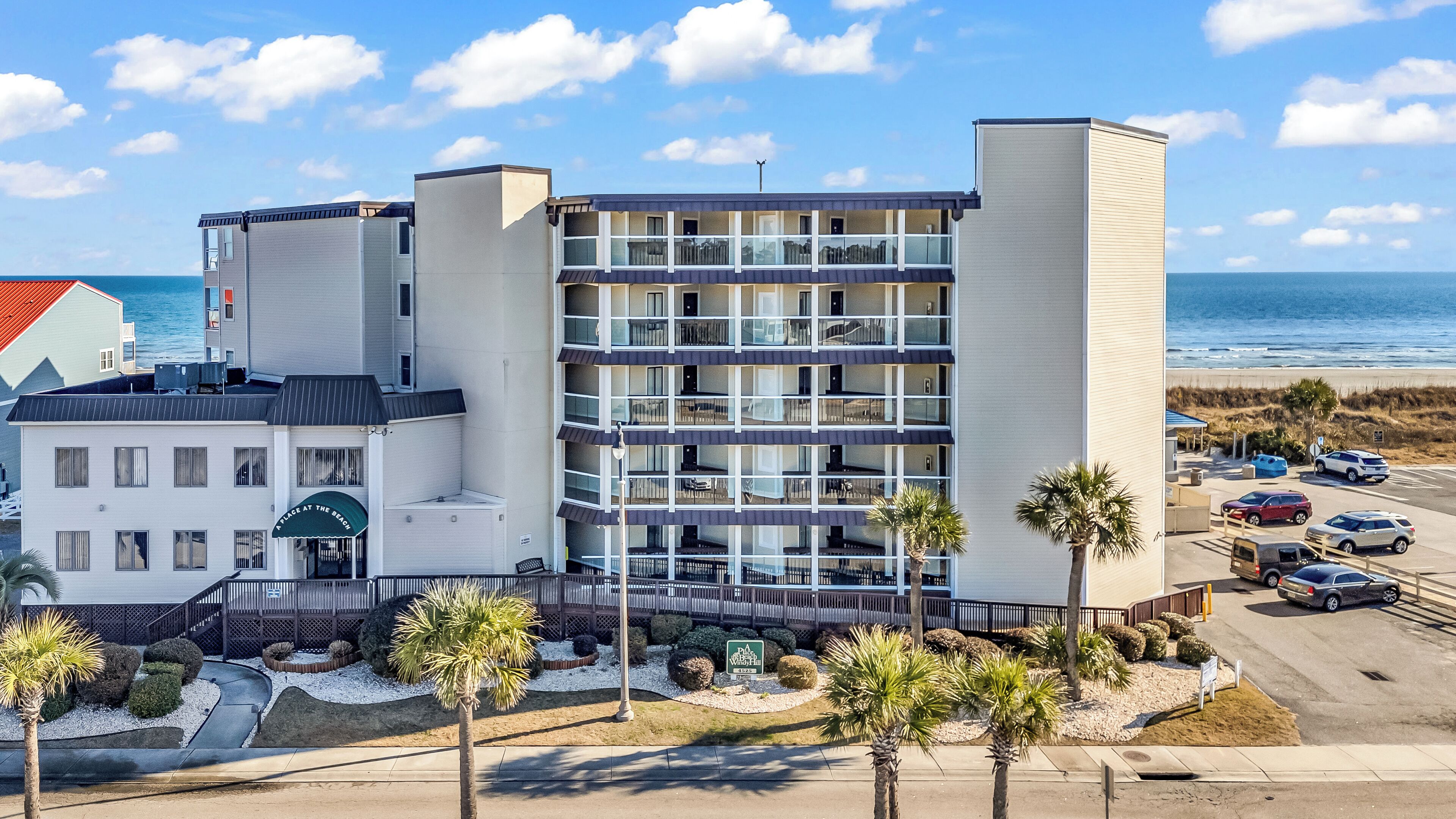 A multi-story hotel with balconies, a beach view, and a parking area with several cars.