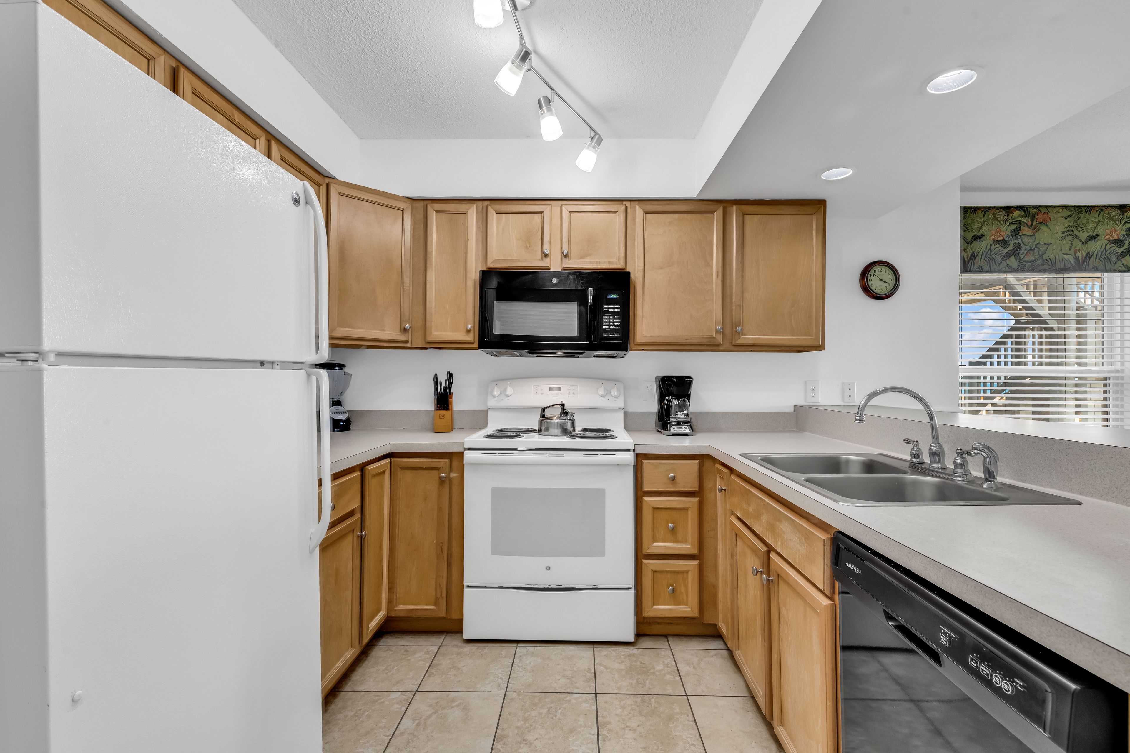 Cocina compacta con armarios de madera, refrigerador blanco, microondas, estufa, cafetera y lavavajillas.