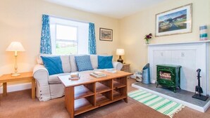 A cozy living room with a sofa, a coffee table, a fireplace, and a window with curtains. - Harbour (Isle of Colonsay)
